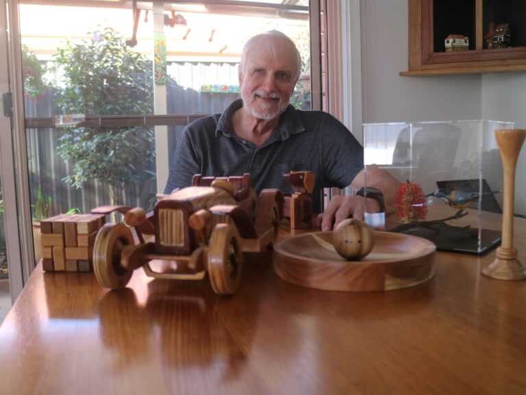 Leigh proudly smiling behind his woodworking projects on a table