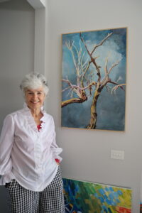 Wendy and her artwork Wendy smiling and standing in front of one of her paintings indoors