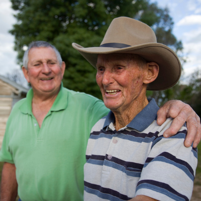 Two people standing outdoors, one resting a supportive hand on the other’s shoulder. They are dressed casually, with one wearing a broad‑brimmed hat, symbolising connection, support, and community—reflecting the spirit of Fight Parkinson’s Peer Support Groups.