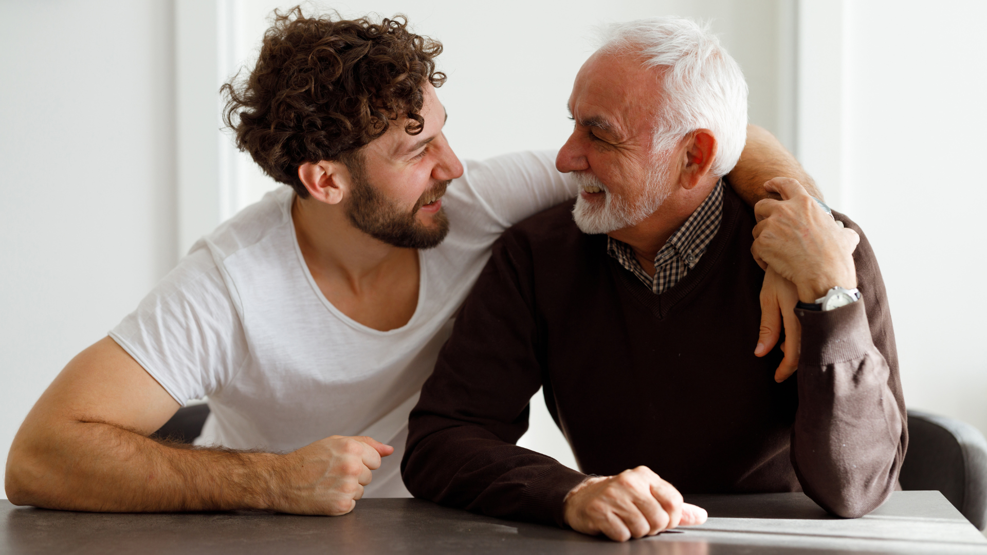 Two people seated at a table, leaning toward each other during a quiet conversation, symbolising trusted support and shared decision‑making when discussing future care wishes.
