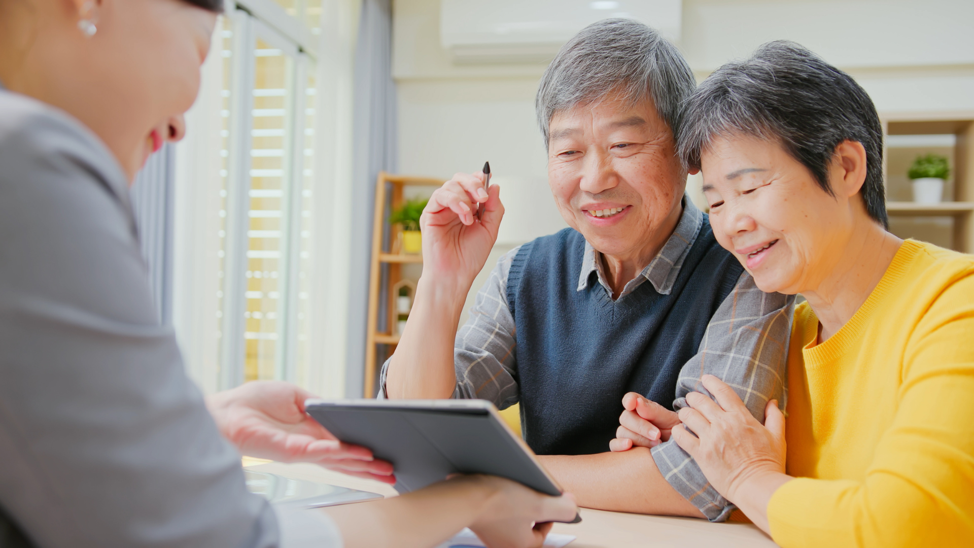 Two people seated at a table reviewing information on a tablet with a health professional, illustrating a discussion about future health care decisions and advance care planning.