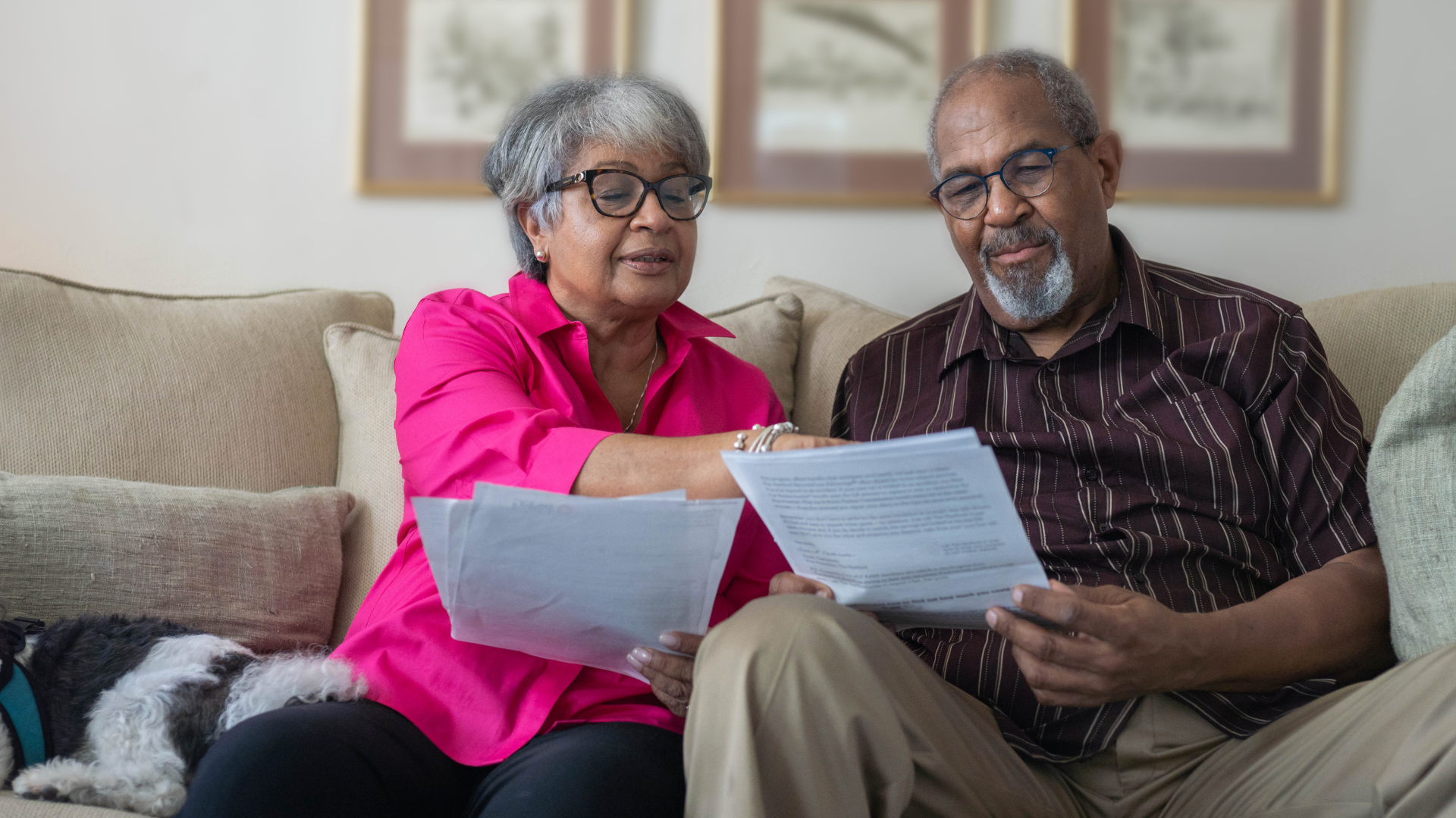 Two people sitting together on a couch reading printed documents, representing the process of reviewing and understanding advance care planning paperwork at home.