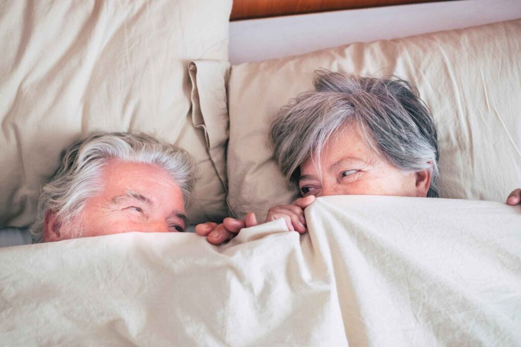 An older couple looking at each other under the sheets