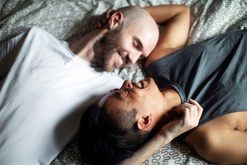 A couple smiling at each other while lying on a bed