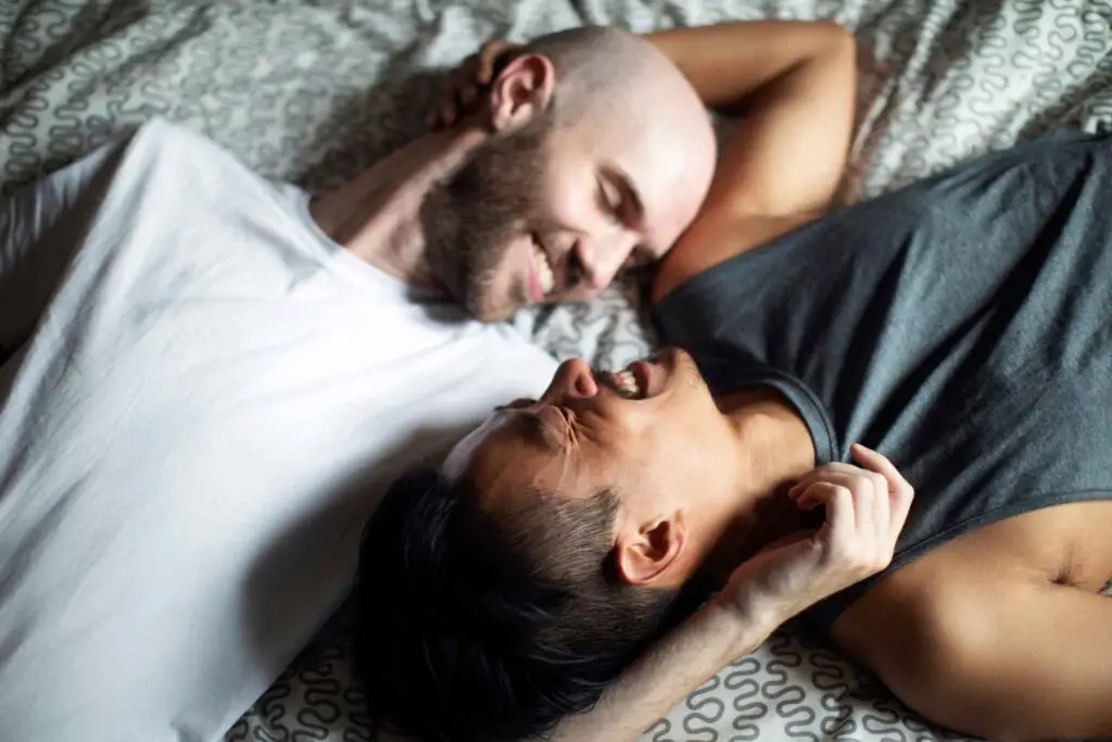 A couple smiling at each other while lying on a bed