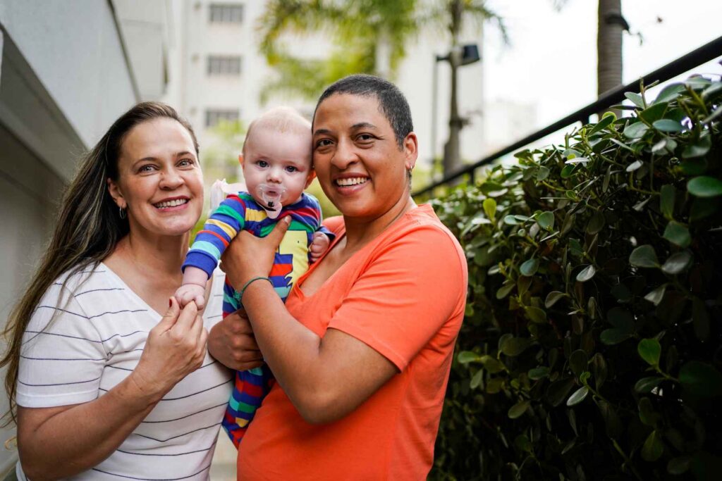 A young couple holding up their baby for a photo during a sunny day