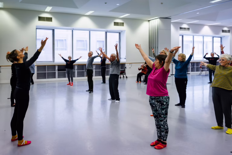 Dance for Parkinson's class with participants mirroring the dance teacher's movements in a studio setting