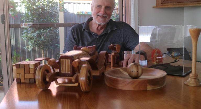 Leigh proudly smiling behind his woodworking projects on a table